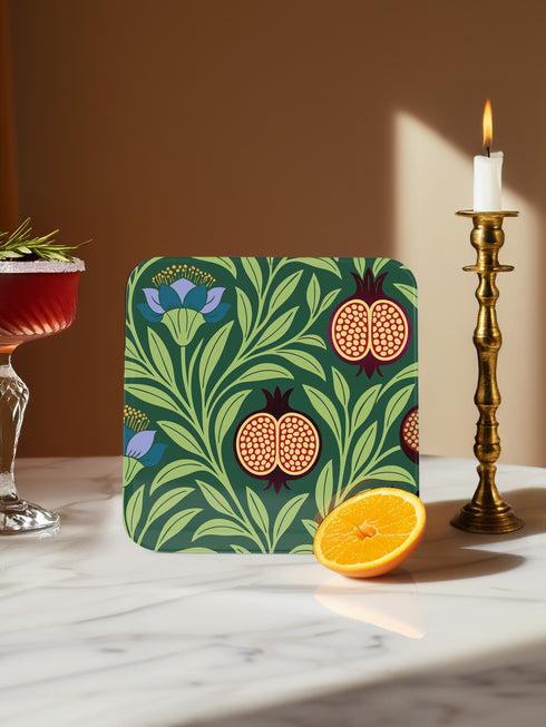 Set of four square drinking coasters featuring rich, dark green botanical illustration with highly detailed Pomegranate fruits and sliced cross-sections. The ornate pattern utilizes deep crimson, opulent gold, and ivory tones, strongly reflecting the stylized Art Nouveau period aesthetic and William Morris textile designs. Crafted from durable, resilient masonite hardboard, this luxury item features a protective high-gloss finish and a non-slip cork base.